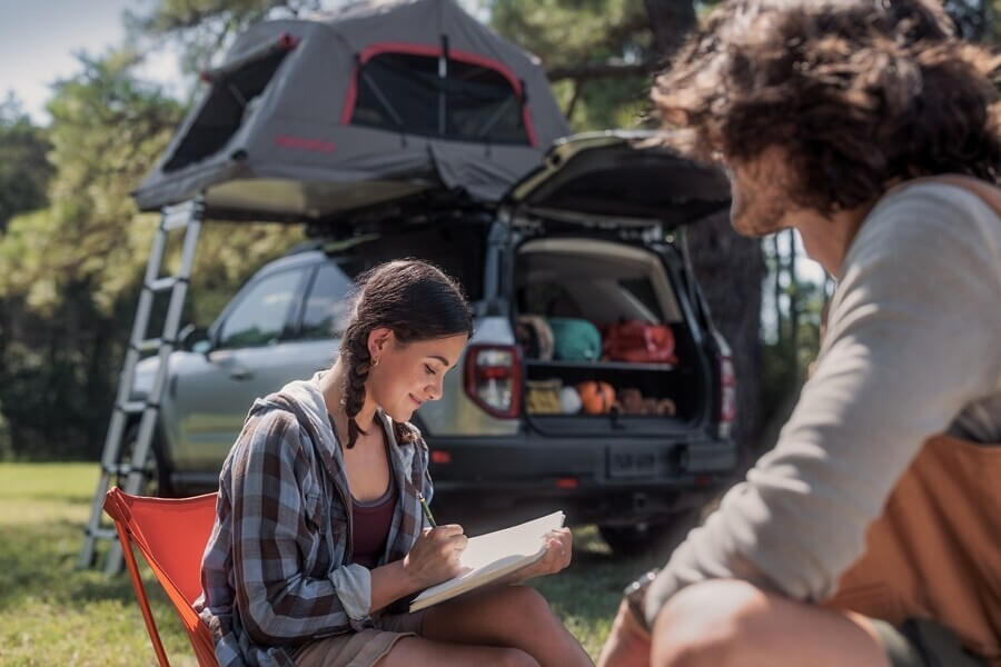A 2024 Ford Bronco® Sport is in the background while a young woman writes in her journal and a man sits near her